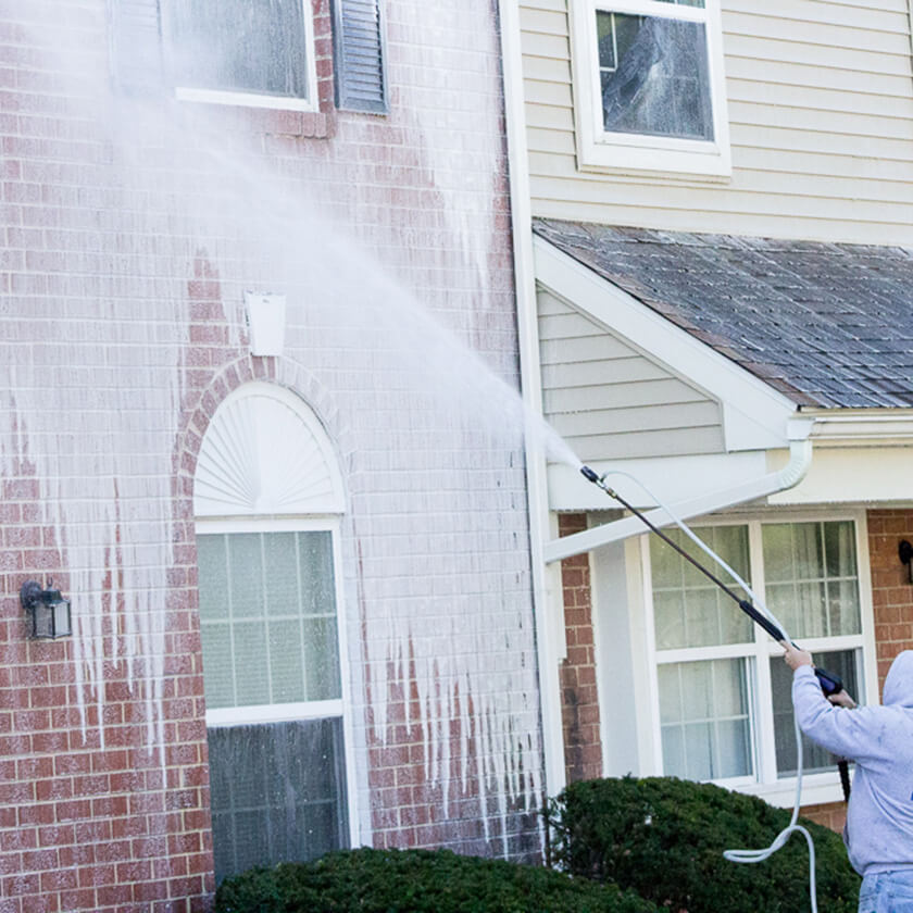Technician soft-washing home siding, visible clean trail